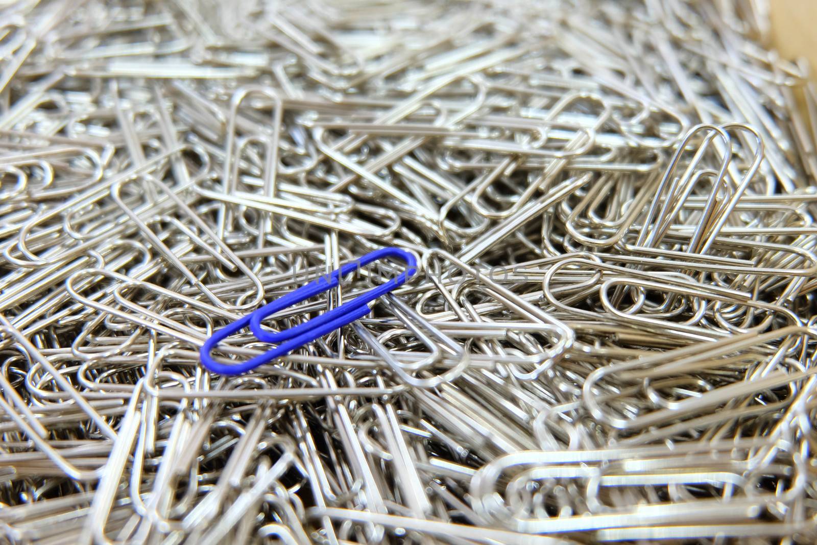Dark blue paper clip on multiple paper clips background.