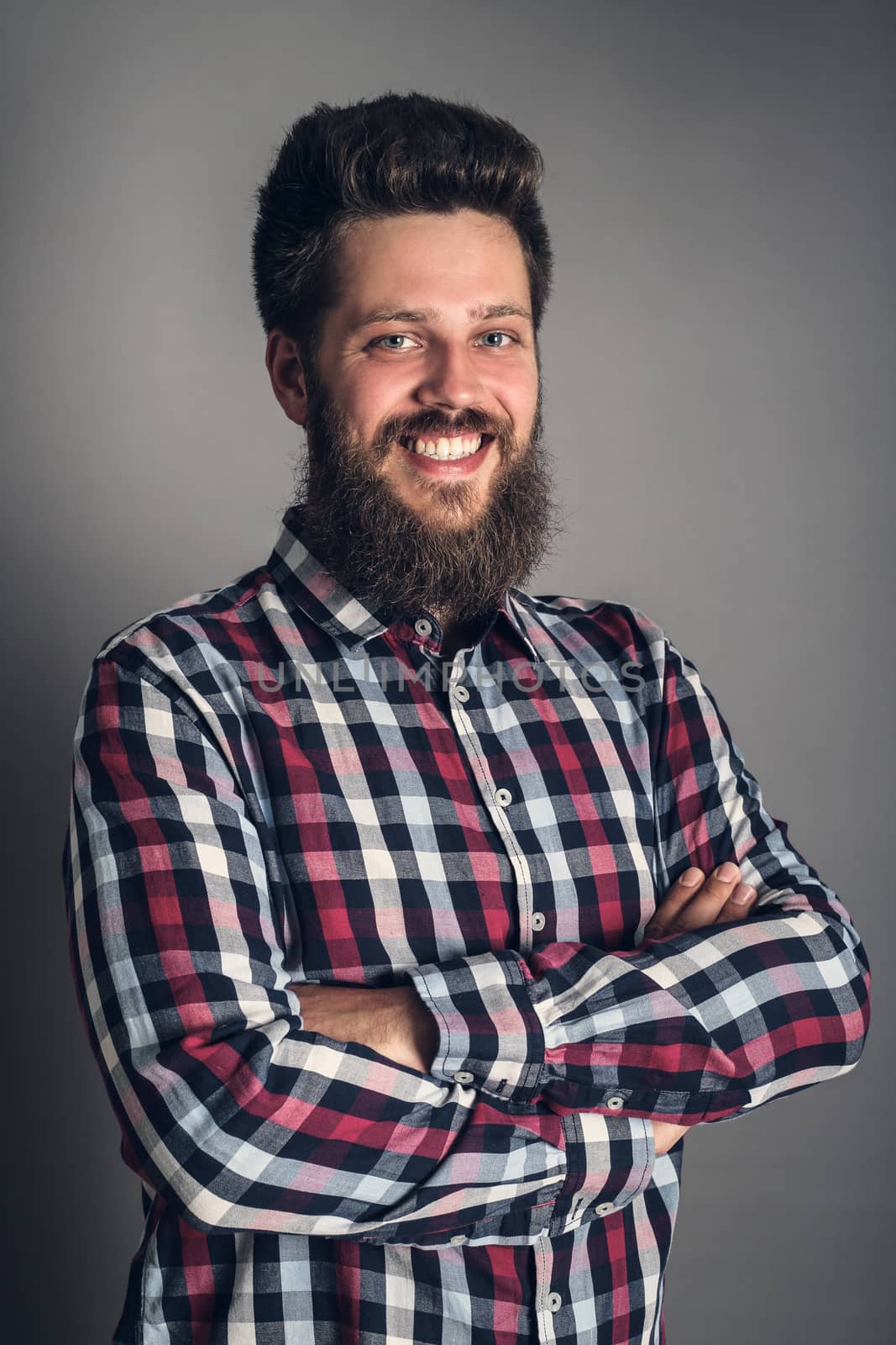 Smiling bearded man in checked shirt, portrait, studio shot on gray background