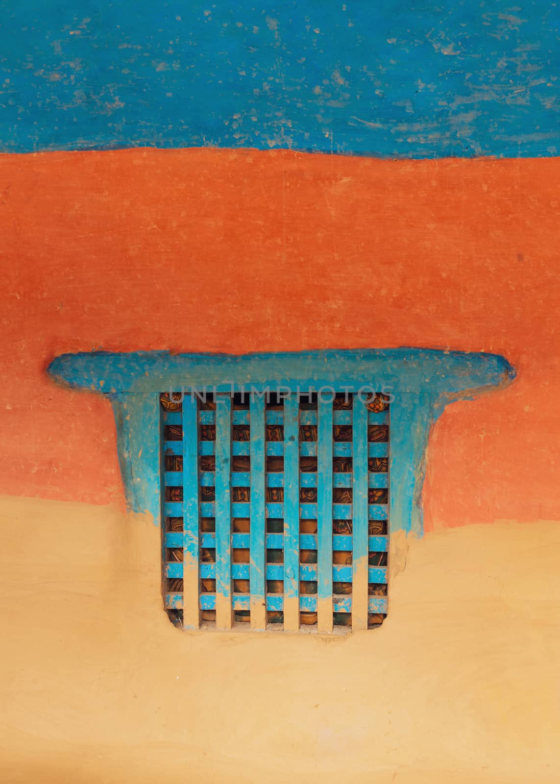 Traditional wooden Nepalese window called Ankhi jhyal. Painted blue on blue, orange and ocher mud wall.