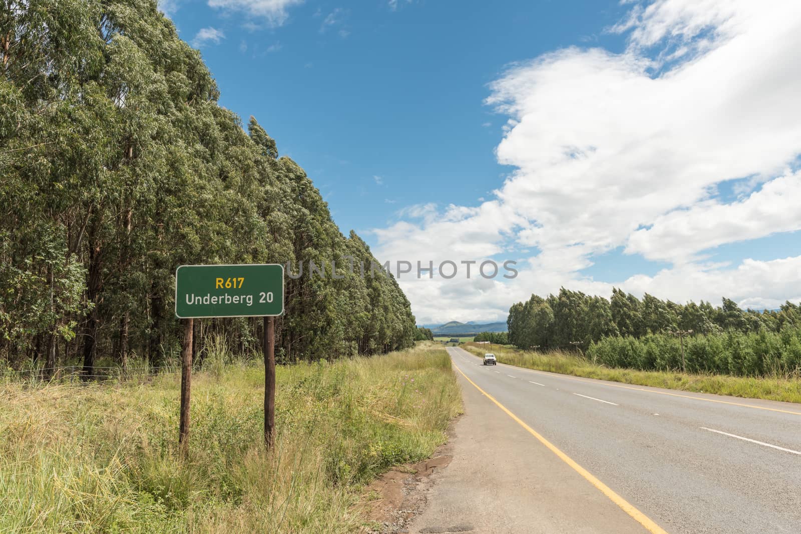 Landscape on road R617 near Underberg in the Kwazulu-Natal Province of South Africa. A distance sign, vehicle and plantation is visible