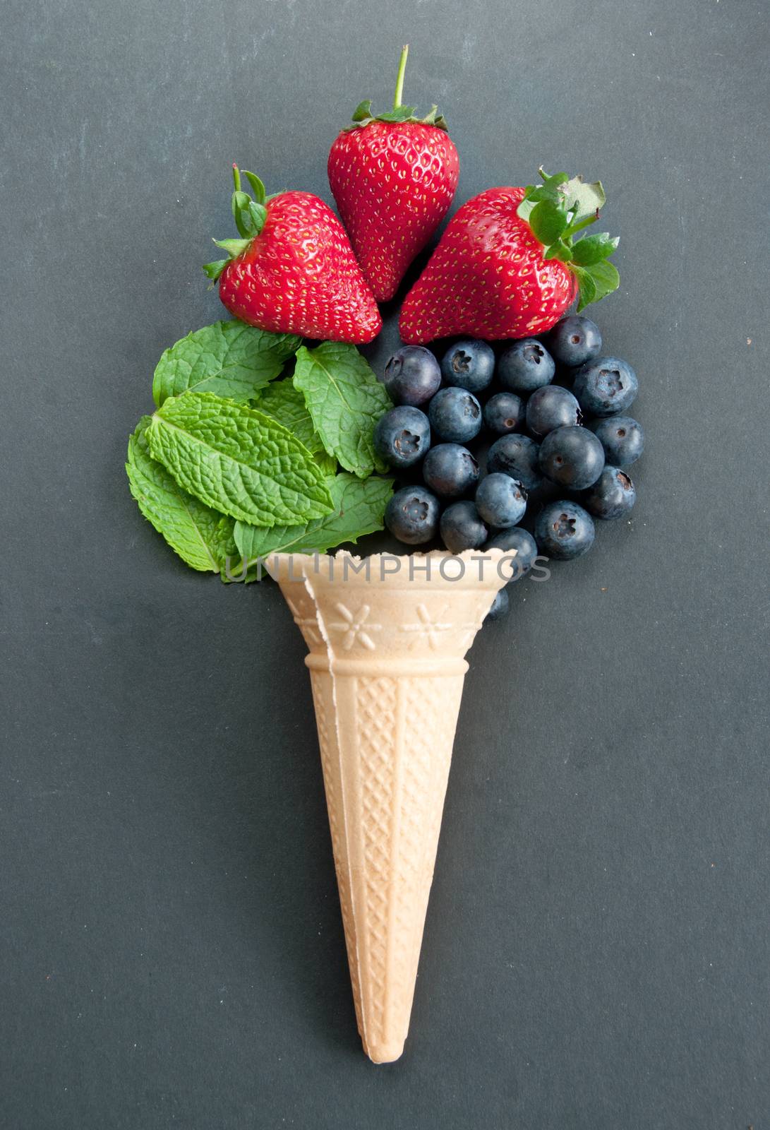 Fresh natural ingredients pouring out of an icecream cone including strawberries, mint and blueberries