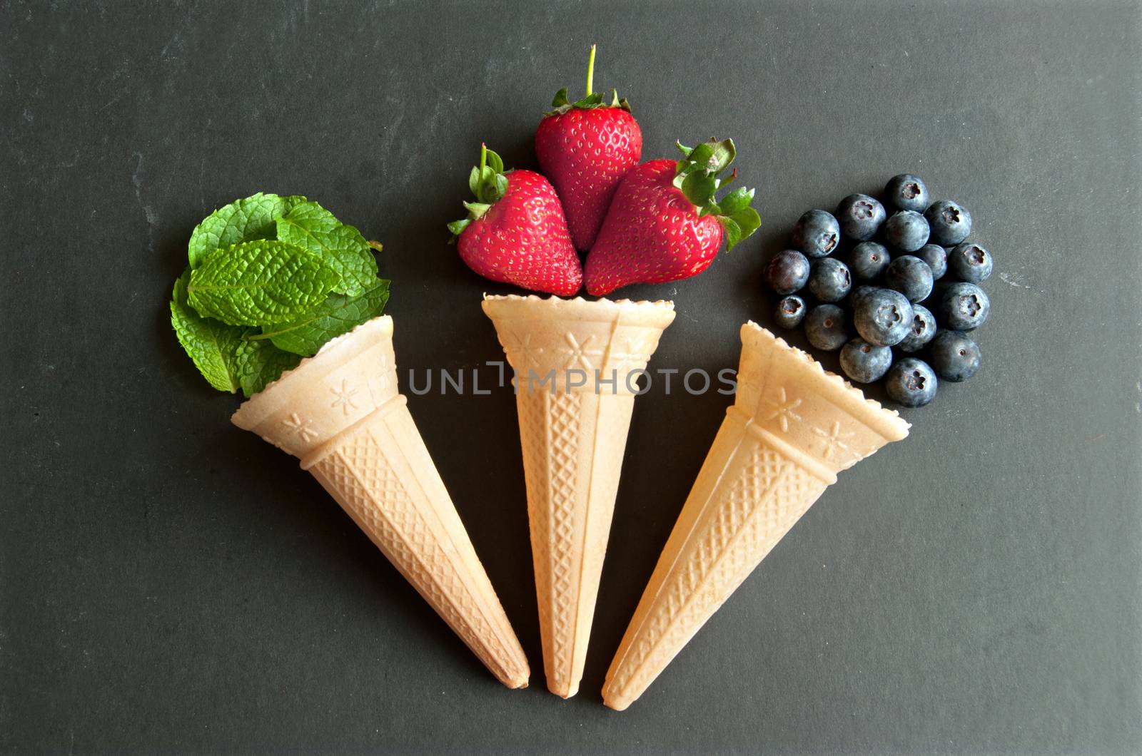 Natural ingredients spilling out of an icecream cone including strawberry, mint and blueberries