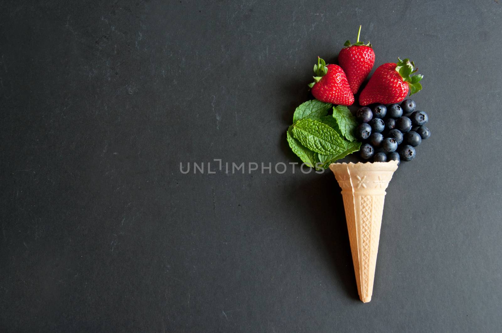Natural ingredients spilling out of an icecream cone including strawberry, mint and blueberries
