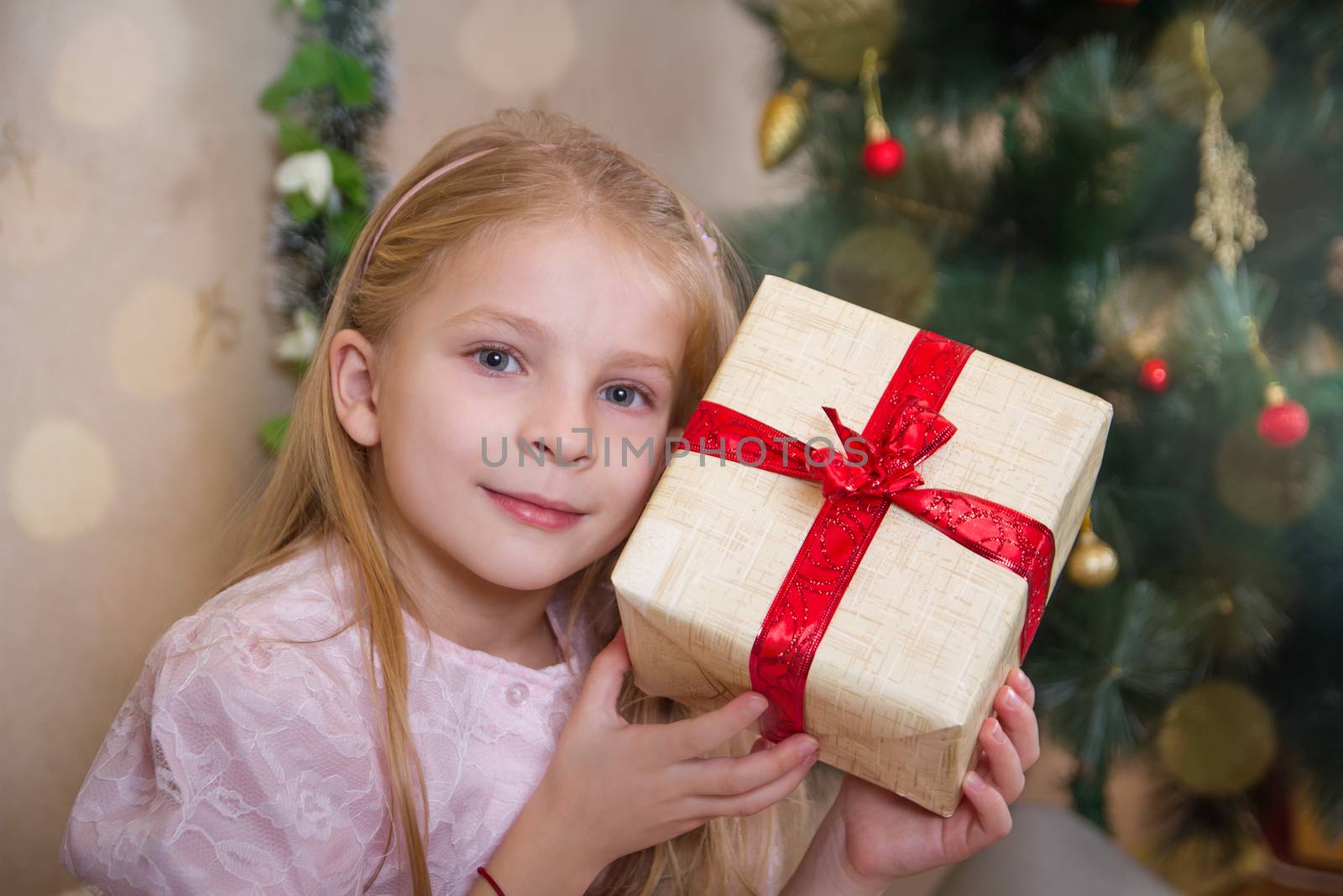 Little girl holding present box near Christmas tree