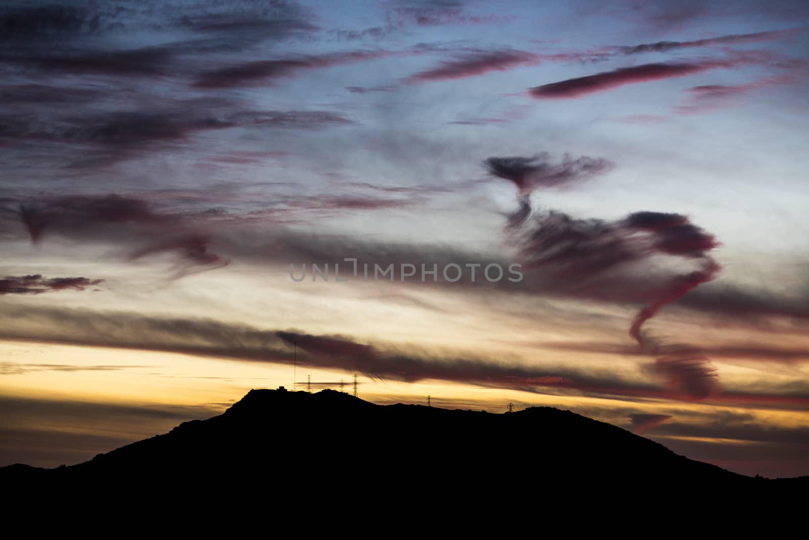 Mountain with powerlines silhoutted by sunset by Njean