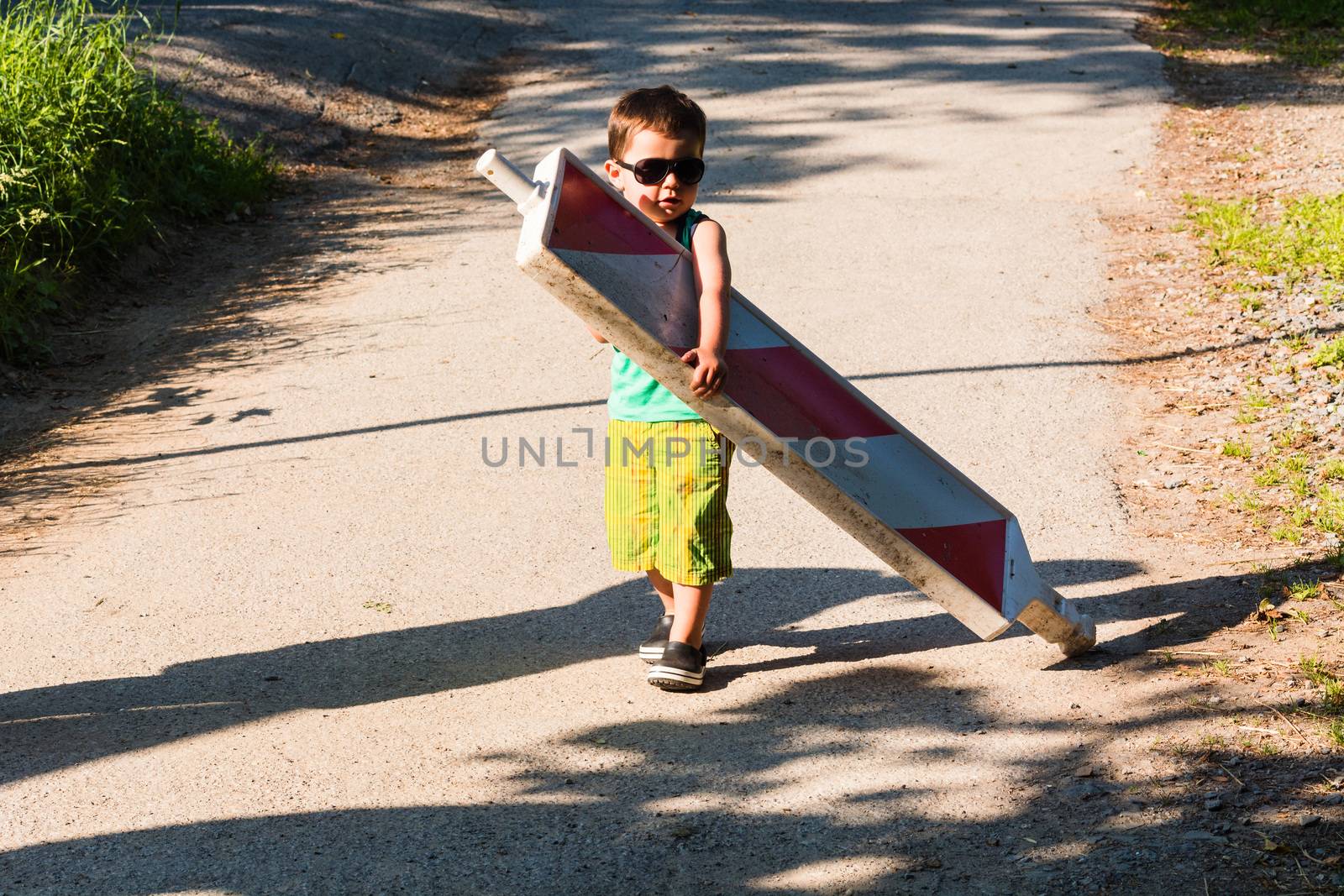 Little boy is carrying a construction site barrier across the street. To overcome difficulties