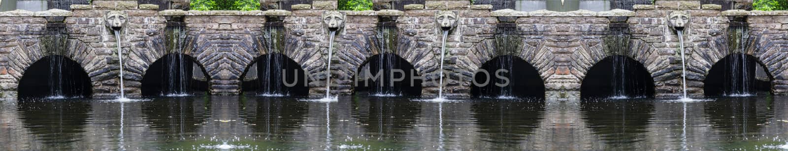 Fountain with waterfall with rock stone decoration in the garden or park. Landscape design detail.