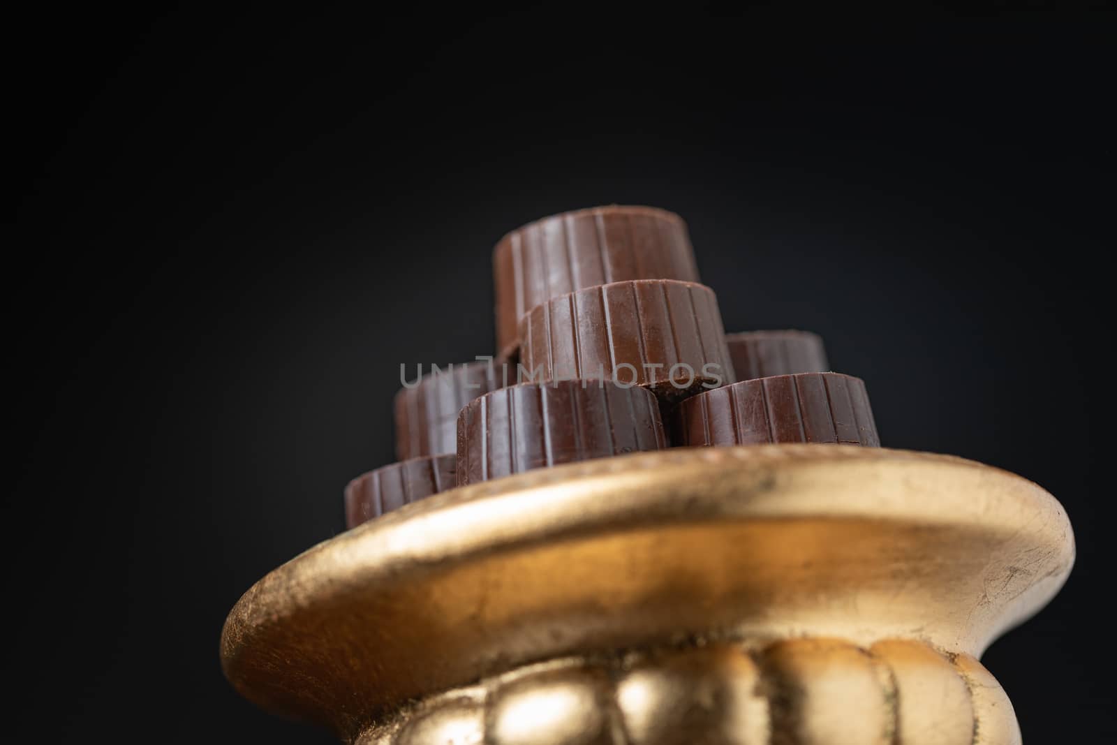 Stack of Fine Chocolates On Golden Pillar Dish With Dark Background.