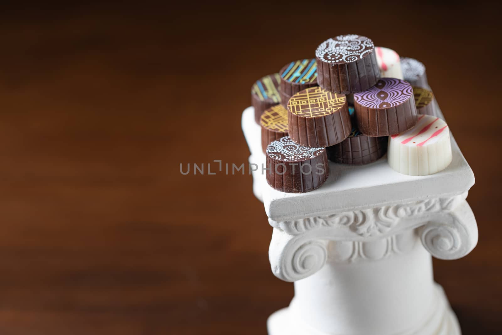 Stack of Fine Artisan Chocolates Stacked On White Pillar Column by Feverpitched