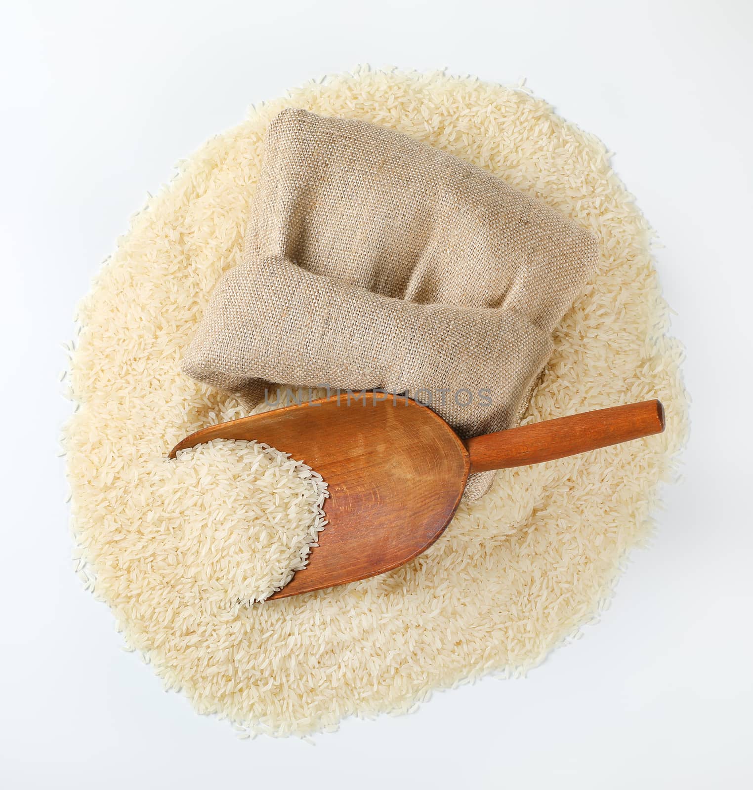 pile of long grained rice, wooden scoop and burlap bag on white background