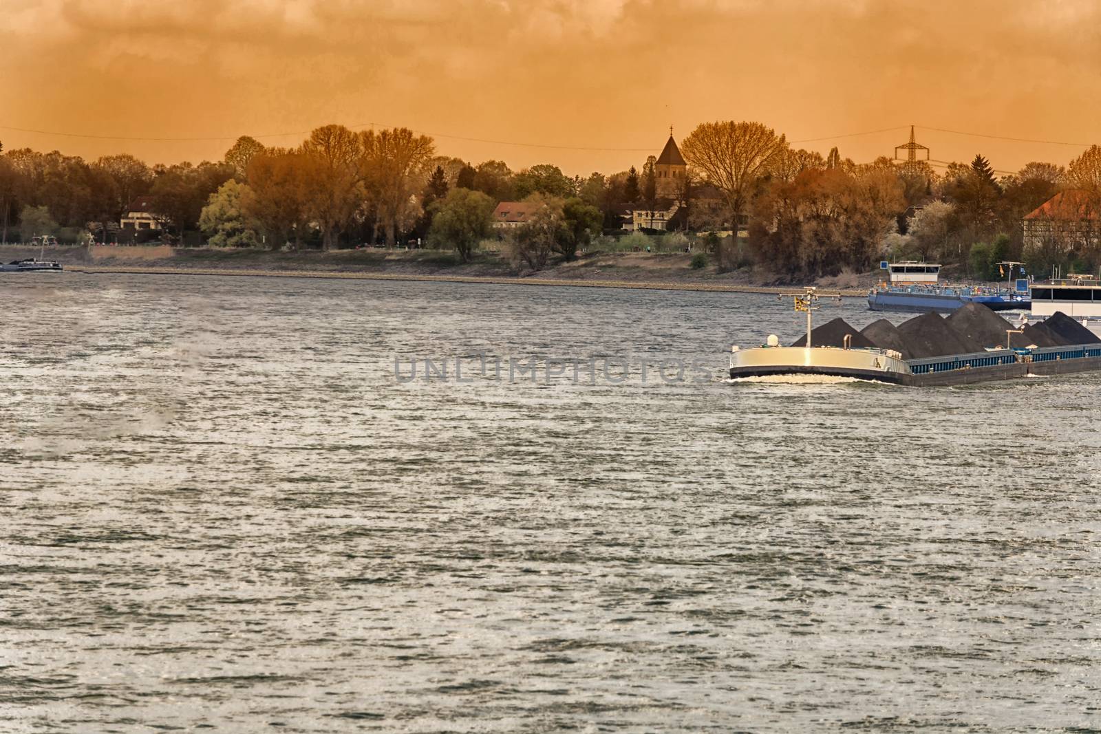 River landscape from the Rhine, near Dusseldorf in Germany. View of the opposite bank and the airport bridge in dramatic sky.