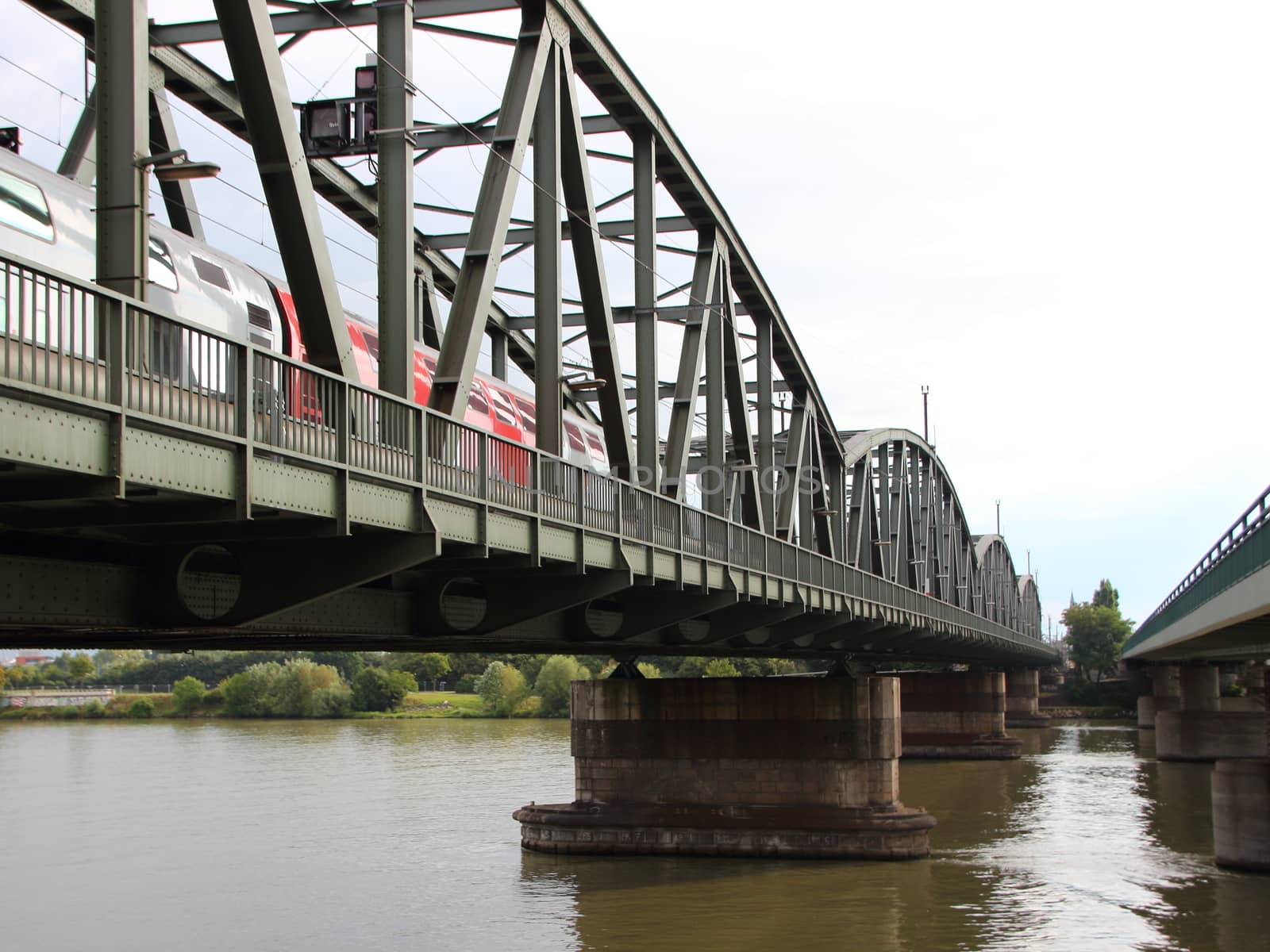 Old Green Metal Railroad Bridge with Red Train Crossing River by HoleInTheBox