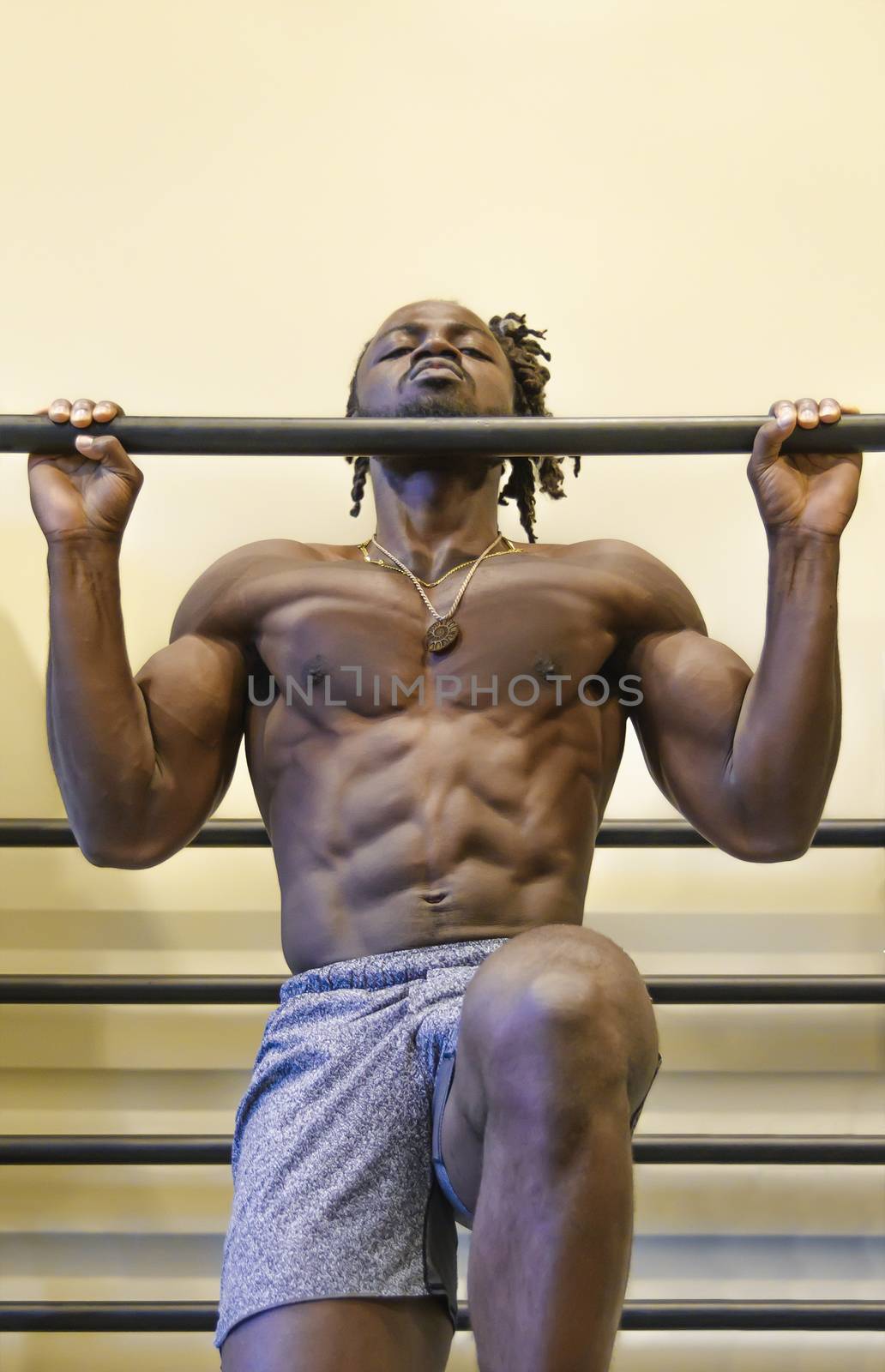 Handsome, young, muscular African American man, a bodybuilder, doing pull-ups in the gym.
