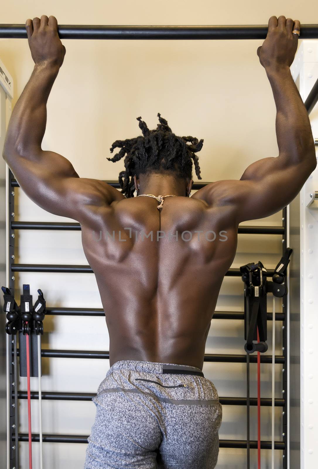 Handsome, young, muscular African American man, a bodybuilder, doing pull-ups in the gym.
