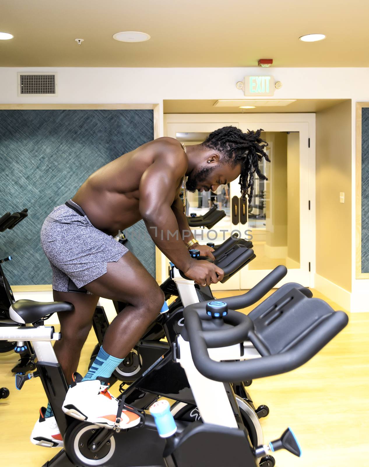 Handsome, young, muscular African American man, a bodybuilder, riding as stationary bicycle in the gym.