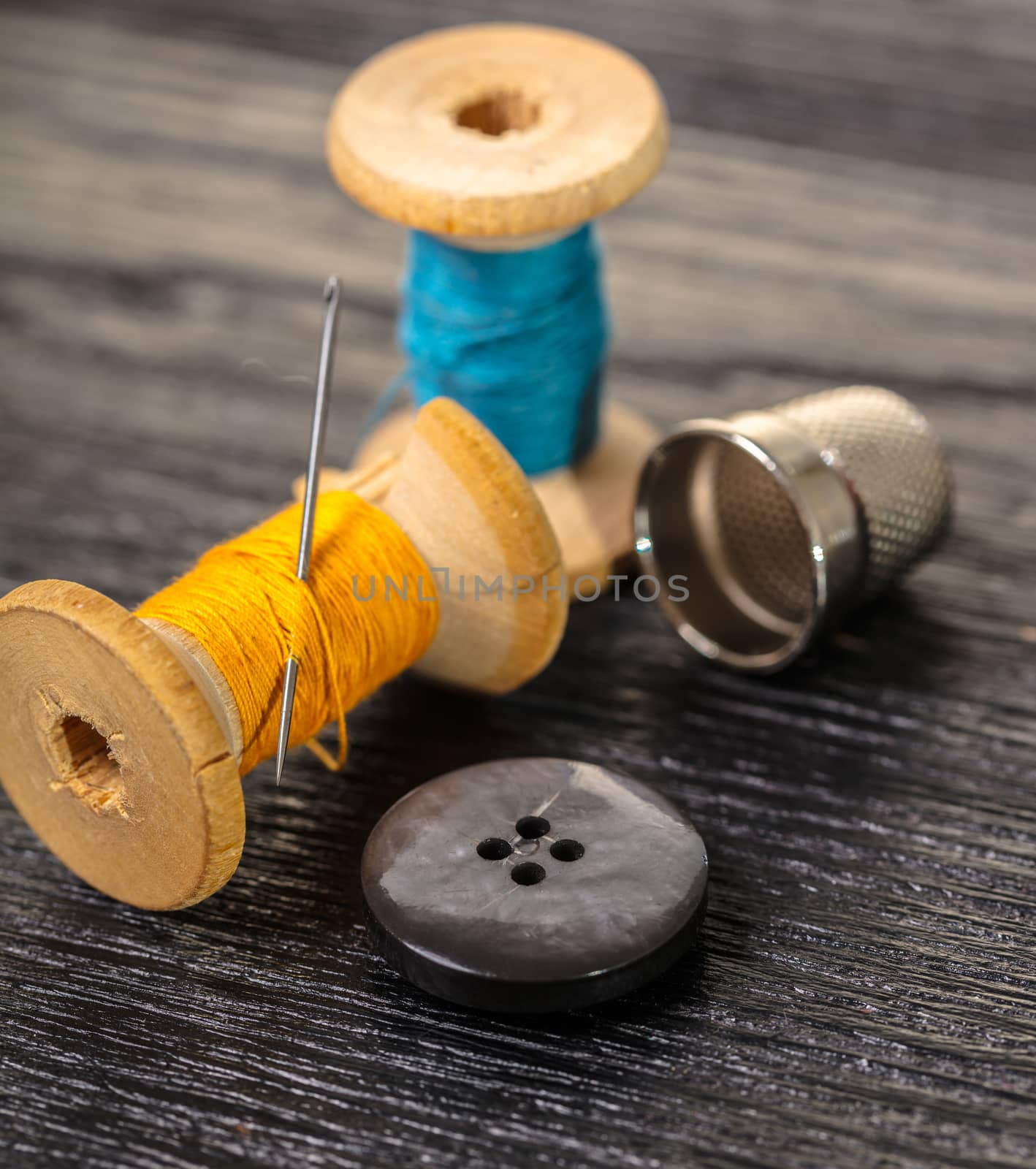 Thread with a thimble and button on black wooden background