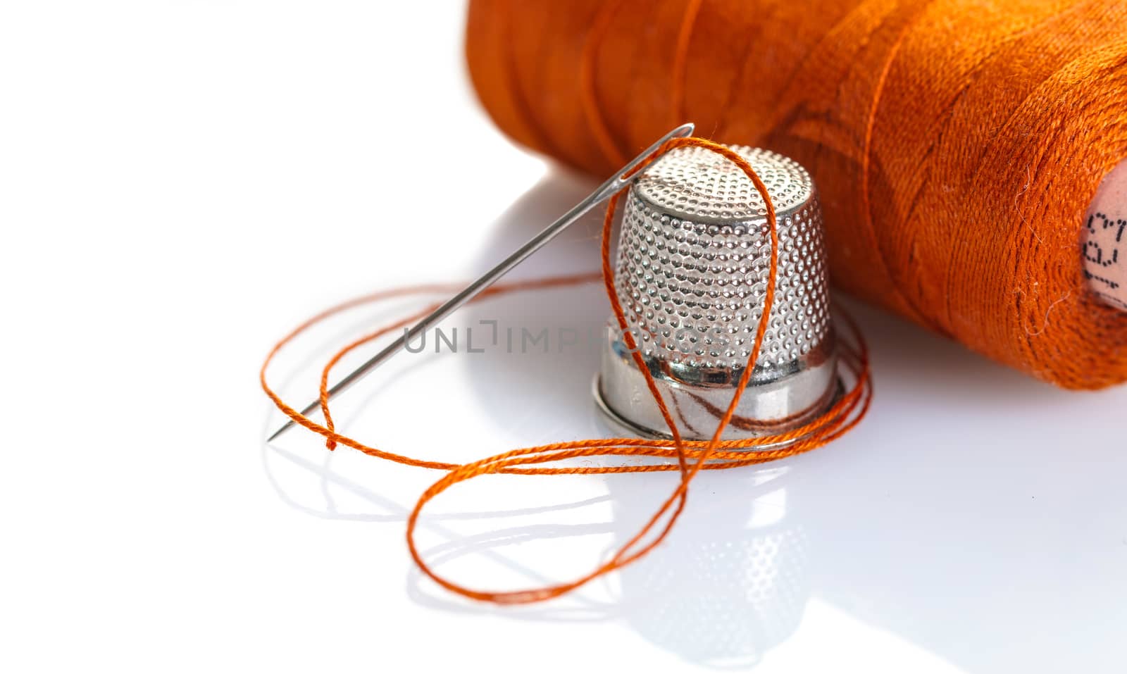 needle with an orange thread and a thimble on white background