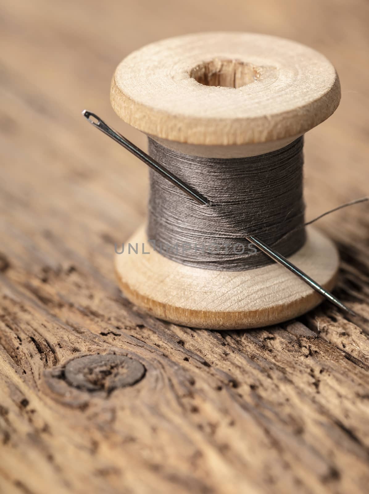 spool of thread with a needle on wooden background