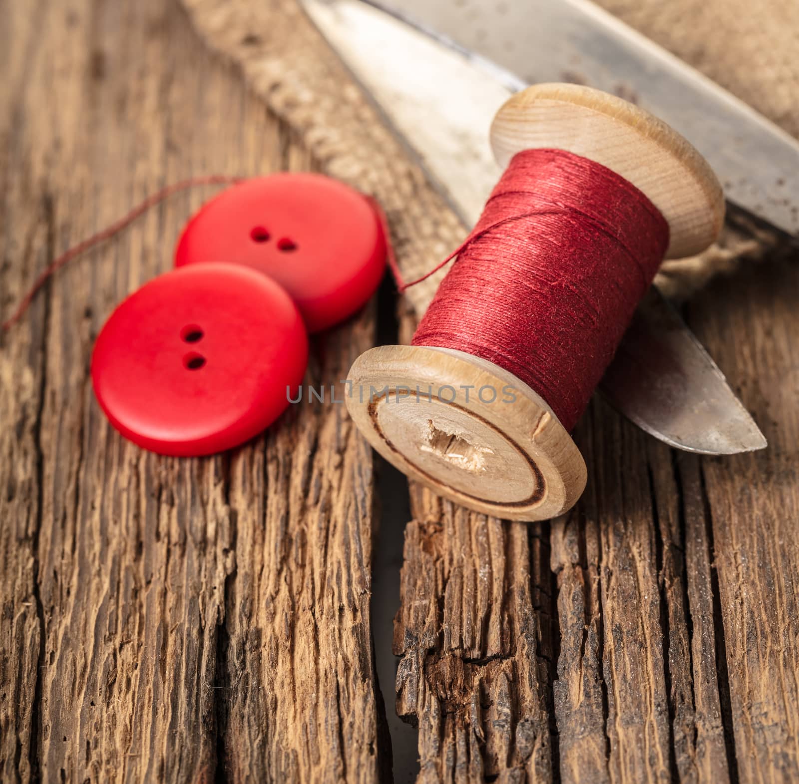 red thread with buttons and scissors, wooden background