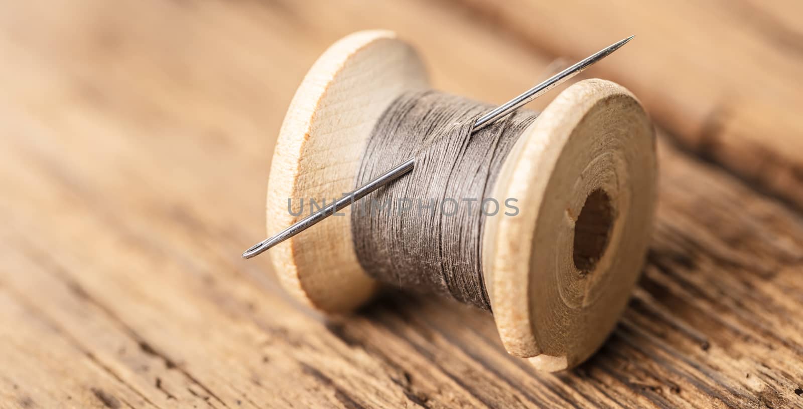 spool of thread with a needle on wooden background
