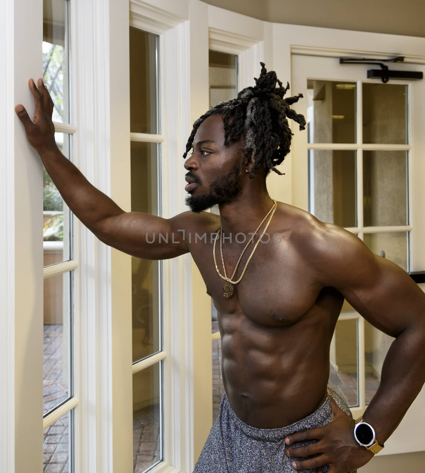 Handsome muscular shirtless African American man looking through the window.