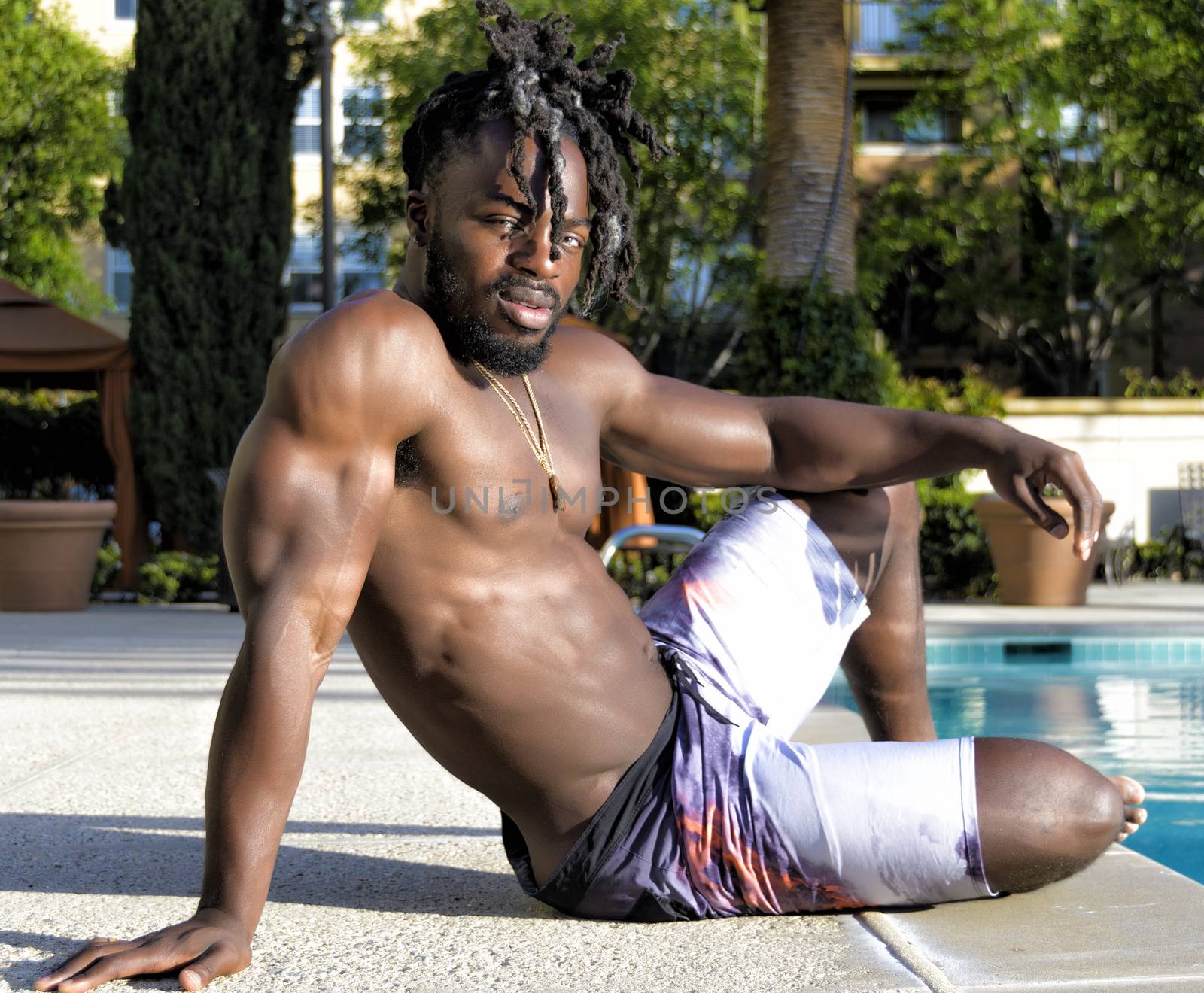 Young handsome shirtless muscular African American man sitting my the pool.