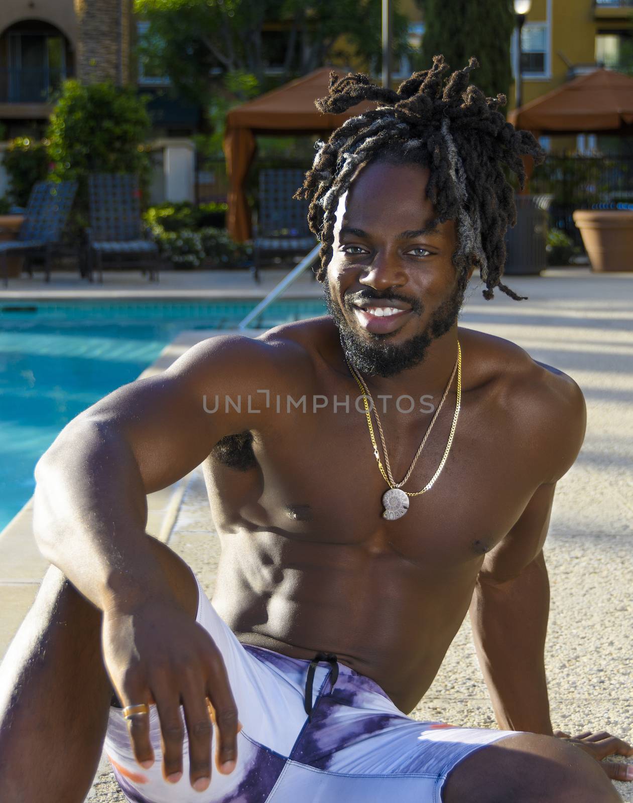 Young handsome shirtless muscular African American man sitting my the pool and smiling.