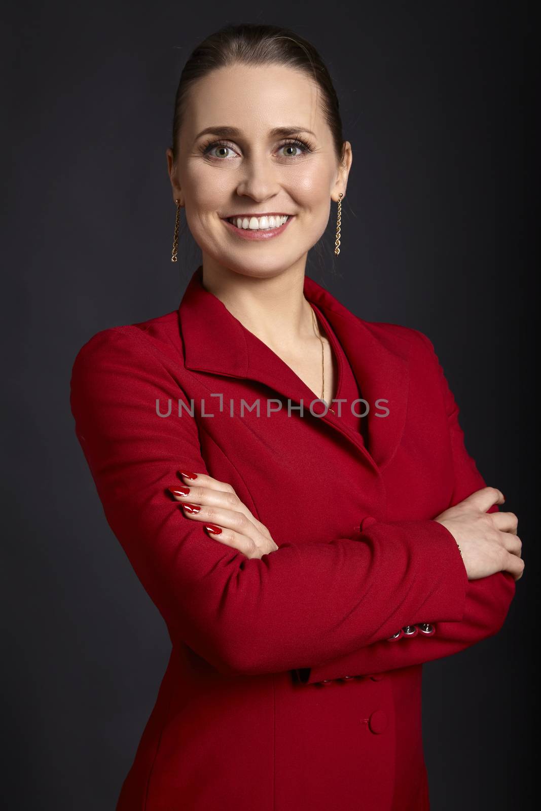 Portrait of elegant young business woman in red jacket with white smile and crossed arms, on black background.