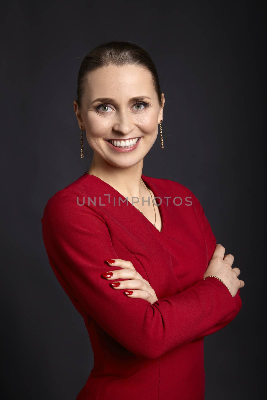 Studio shot of young woman with white smile and crossed arms on black background.