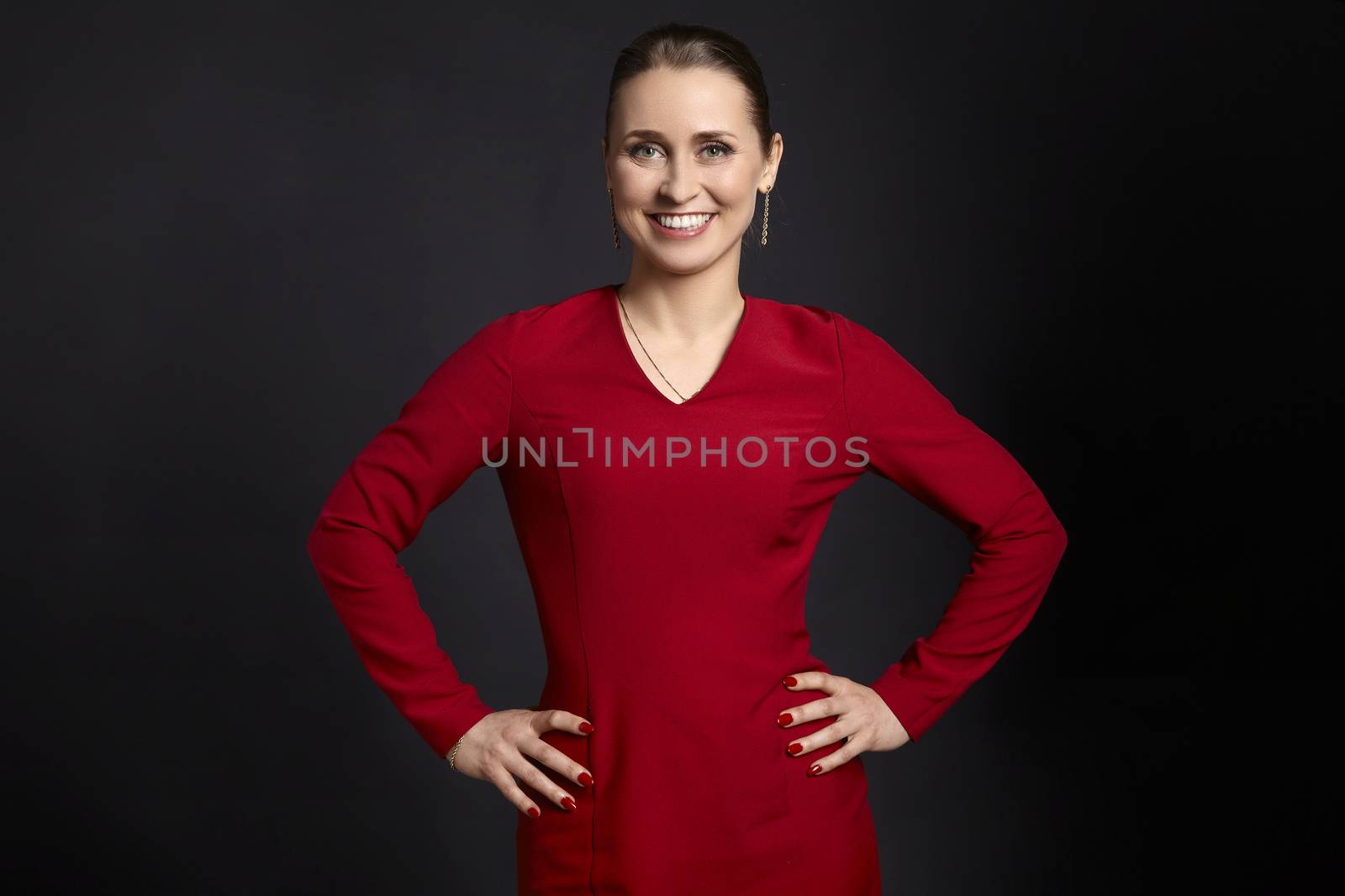 Studio shot of young woman with white smile and hands on hips, on black background.