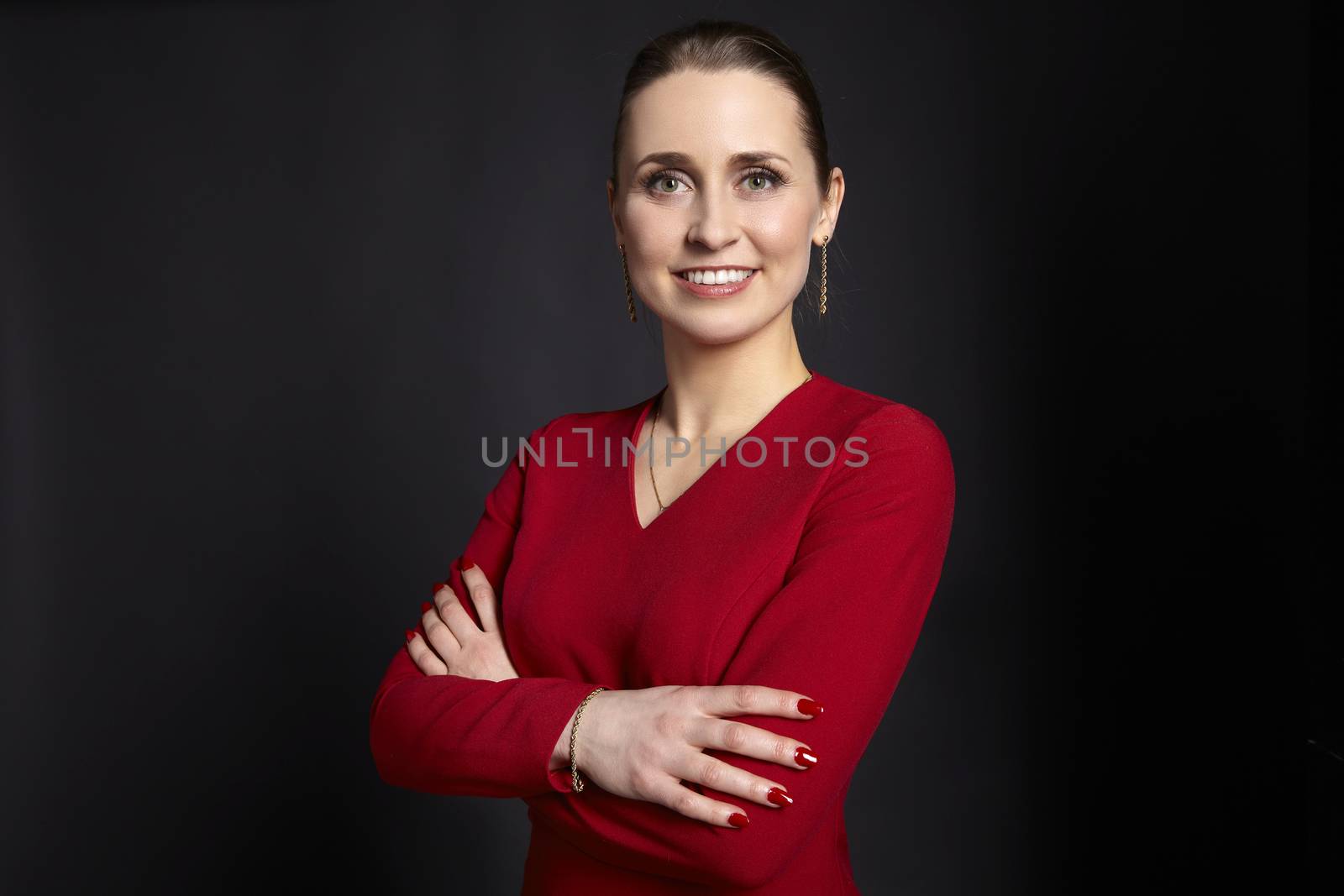 Studio shot of confident young business woman with crossed arms and toothy smile on black background.