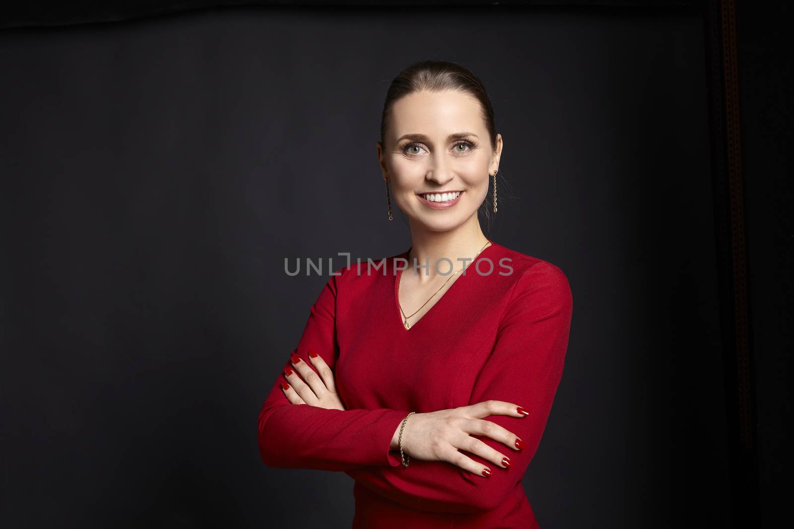 Business portrait of young woman in red dress and arms crossed on black background.
