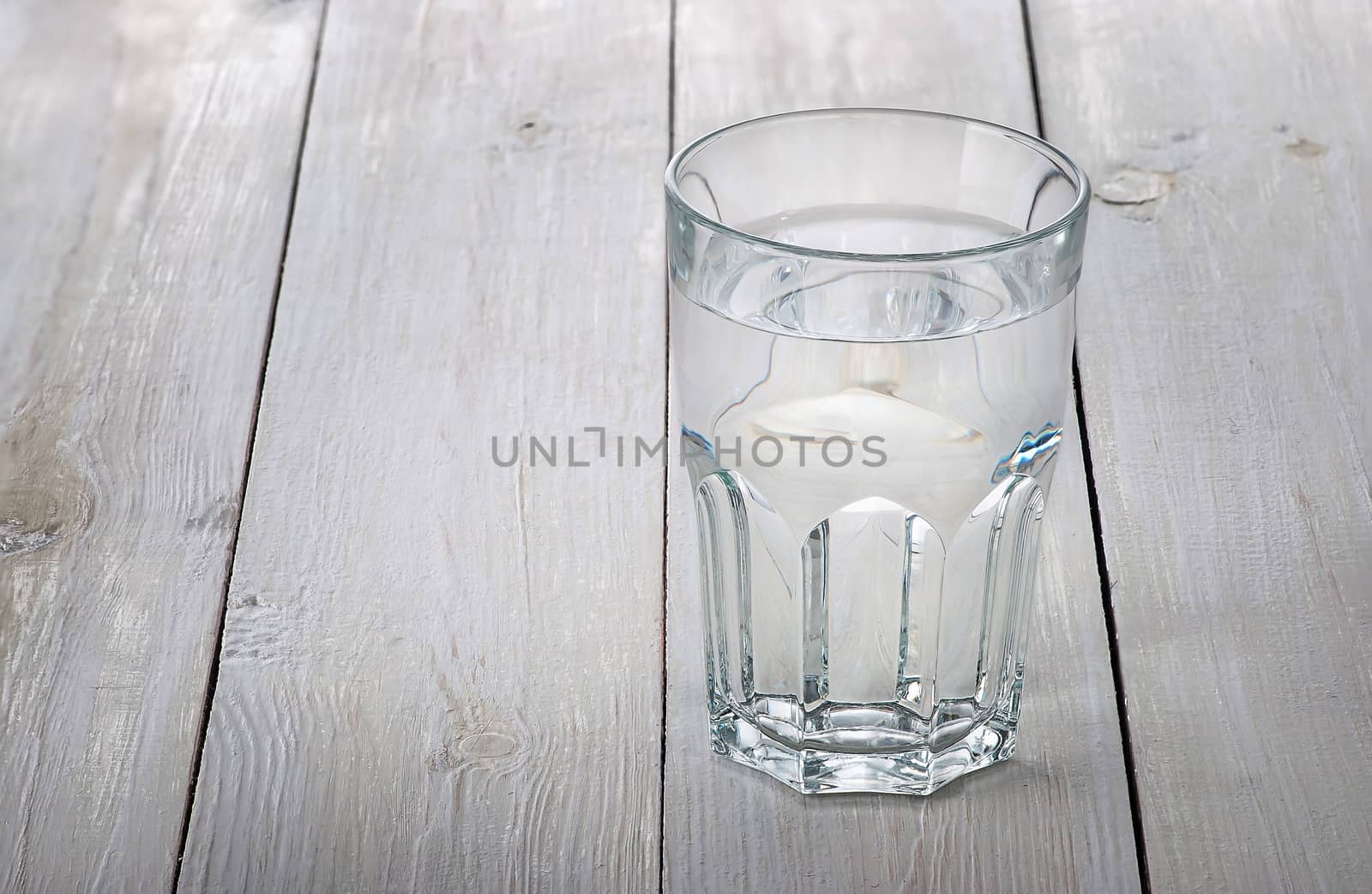 A glass of water on a white wooden table. Blurred background.