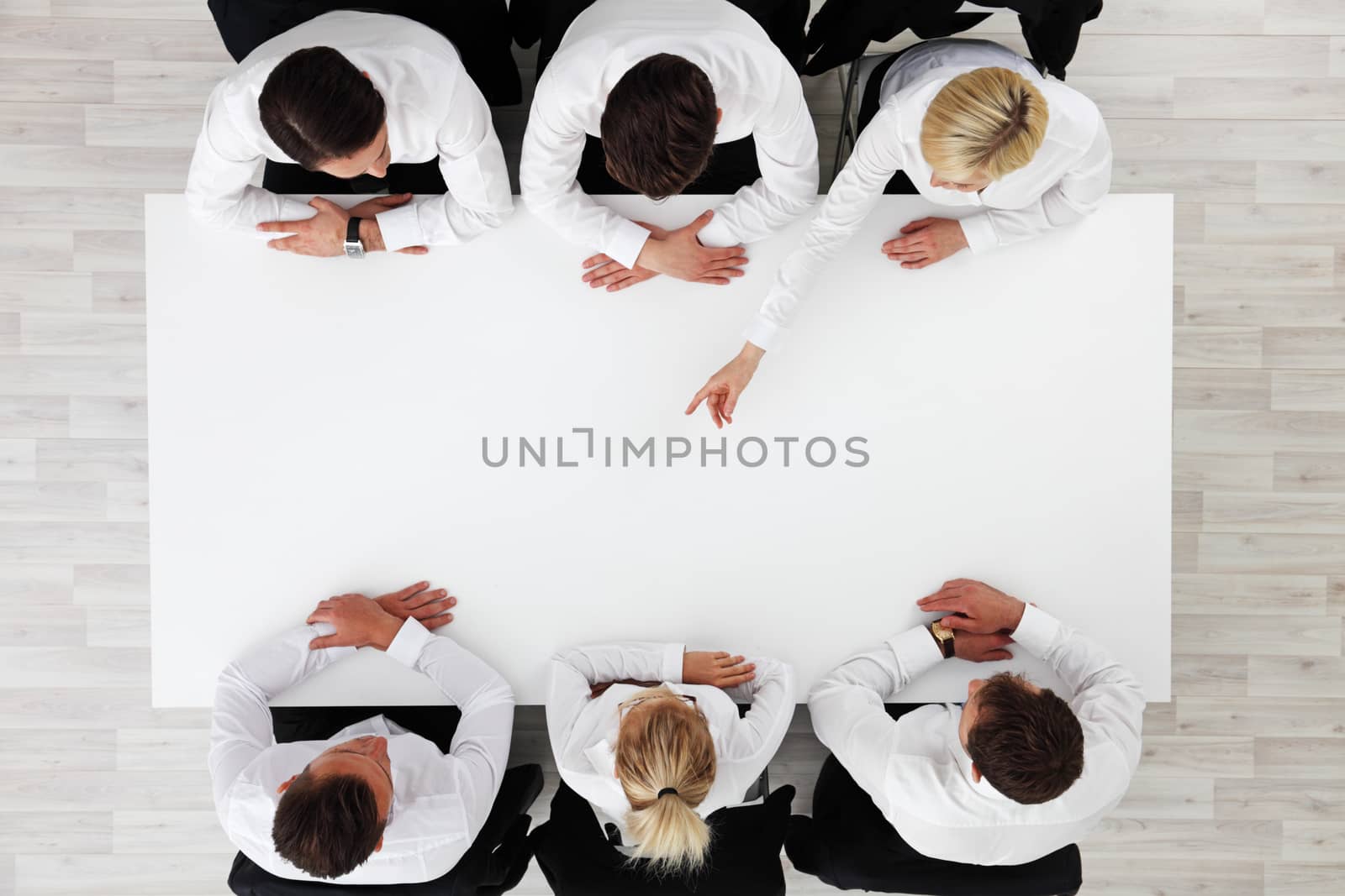 Business people sitting around empty table, business woman pointing to blank copy space in the middle