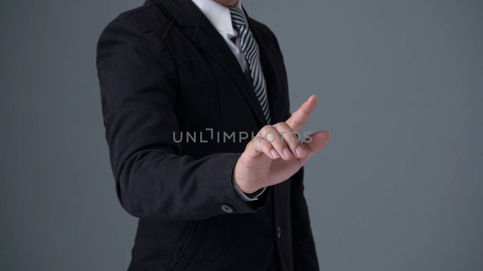 Businessman wearing a black suite pointing finger on gray background