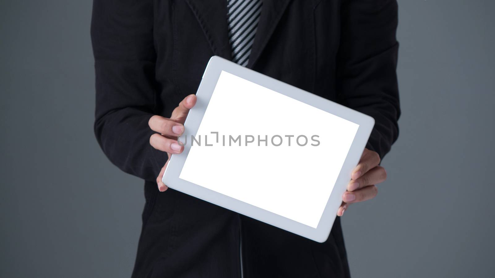 Businessman holding tablet in black suit on gray background
