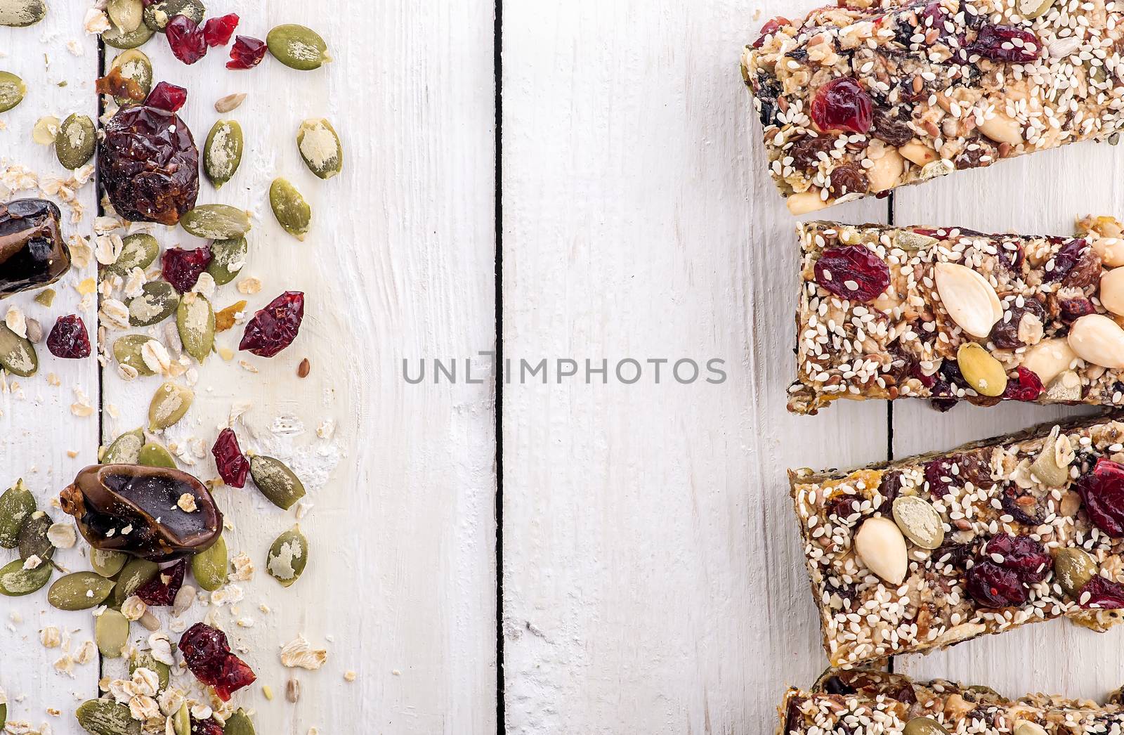 Granola bar with ingredients. Healthy sweet dessert snack. Cereal granola bar with nuts, fruit and berries on a white wooden table. Top view.