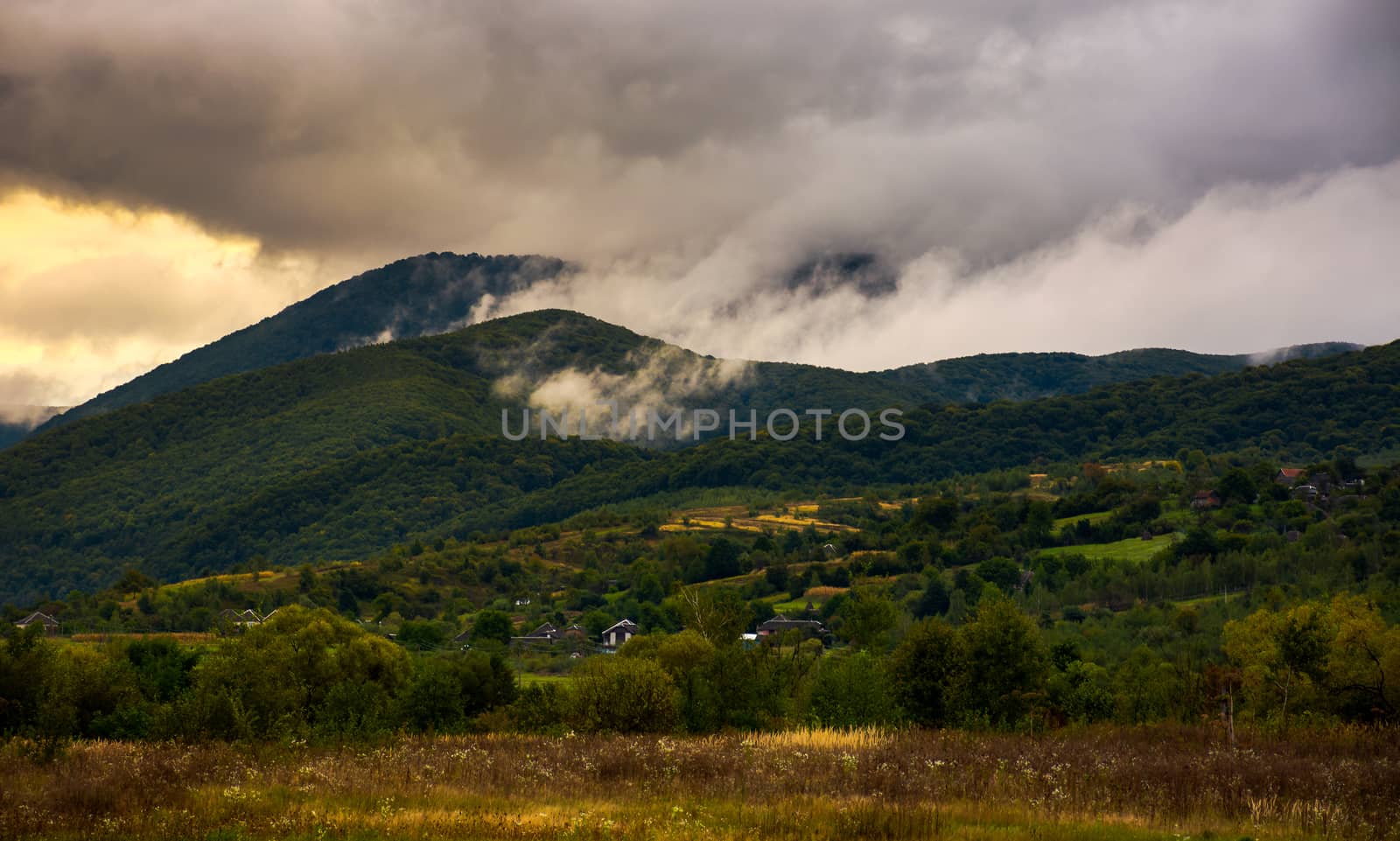 rising clouds in mountainous countryside at menacing sunrise. village at the foot of the mountain. rainy weather