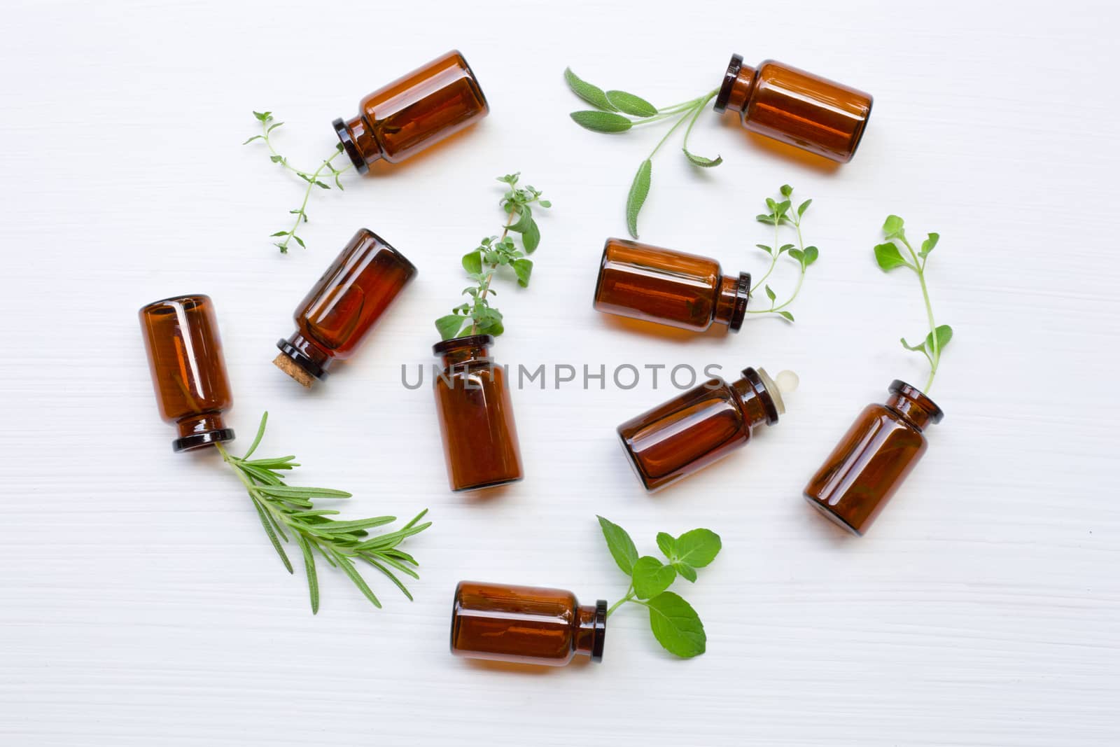 Top view, Bottle of essential oil with herbs on white.