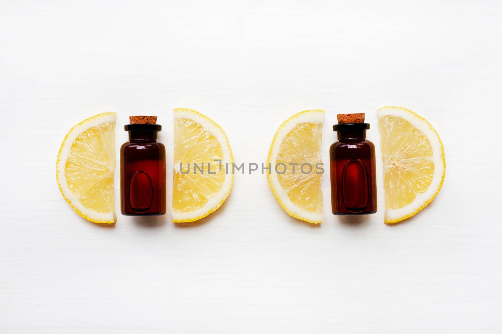 Lemon slices with bottle of lemon essential oil on a white background.