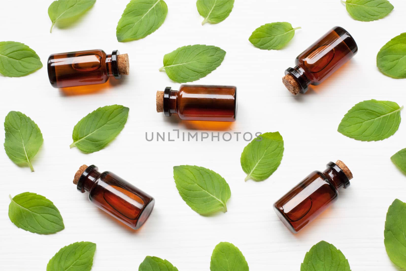 Mint Essential Oil in a Glass Bottle with leaves on white background.