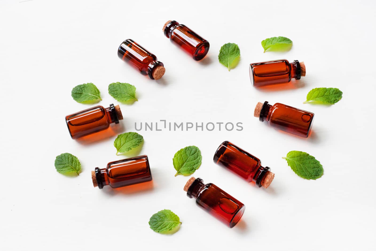 Mint Essential Oil in a Glass Bottle with leaves on white background.