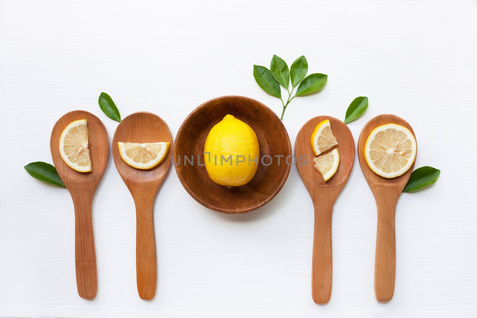 Lemon on wooden bowl and lemon slices on wooden spoon with leaf isolated on white background, top view