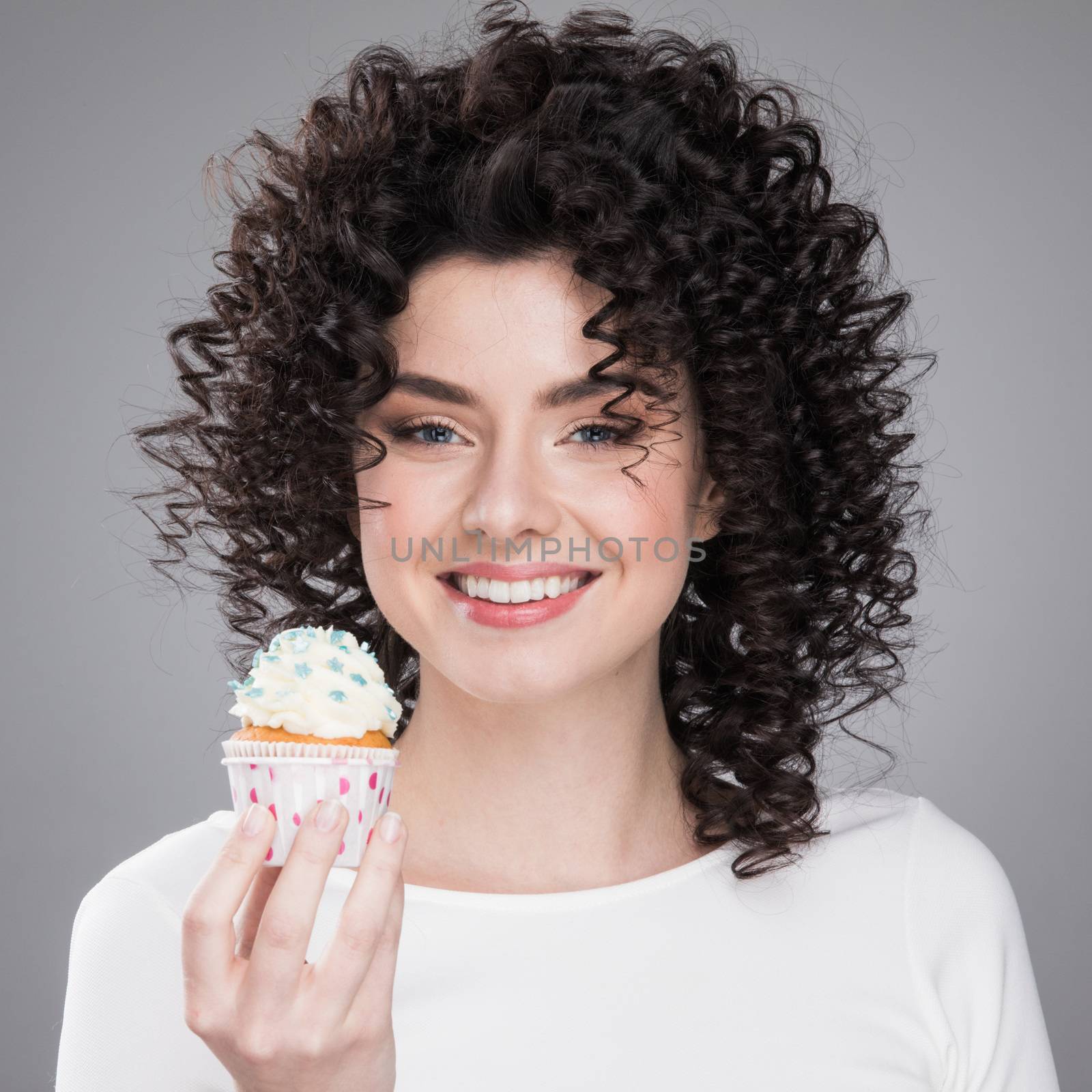 Happy cute lovely curly young woman with curly hair holding cupcake and smiling