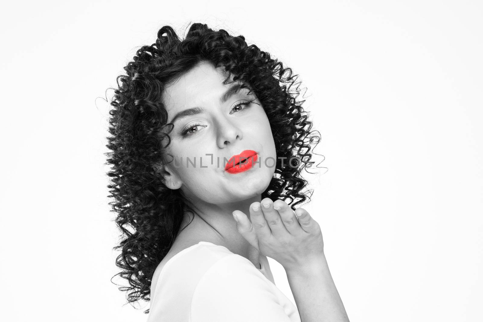 Pretty young woman with curly hair sending air kiss isolated over white background