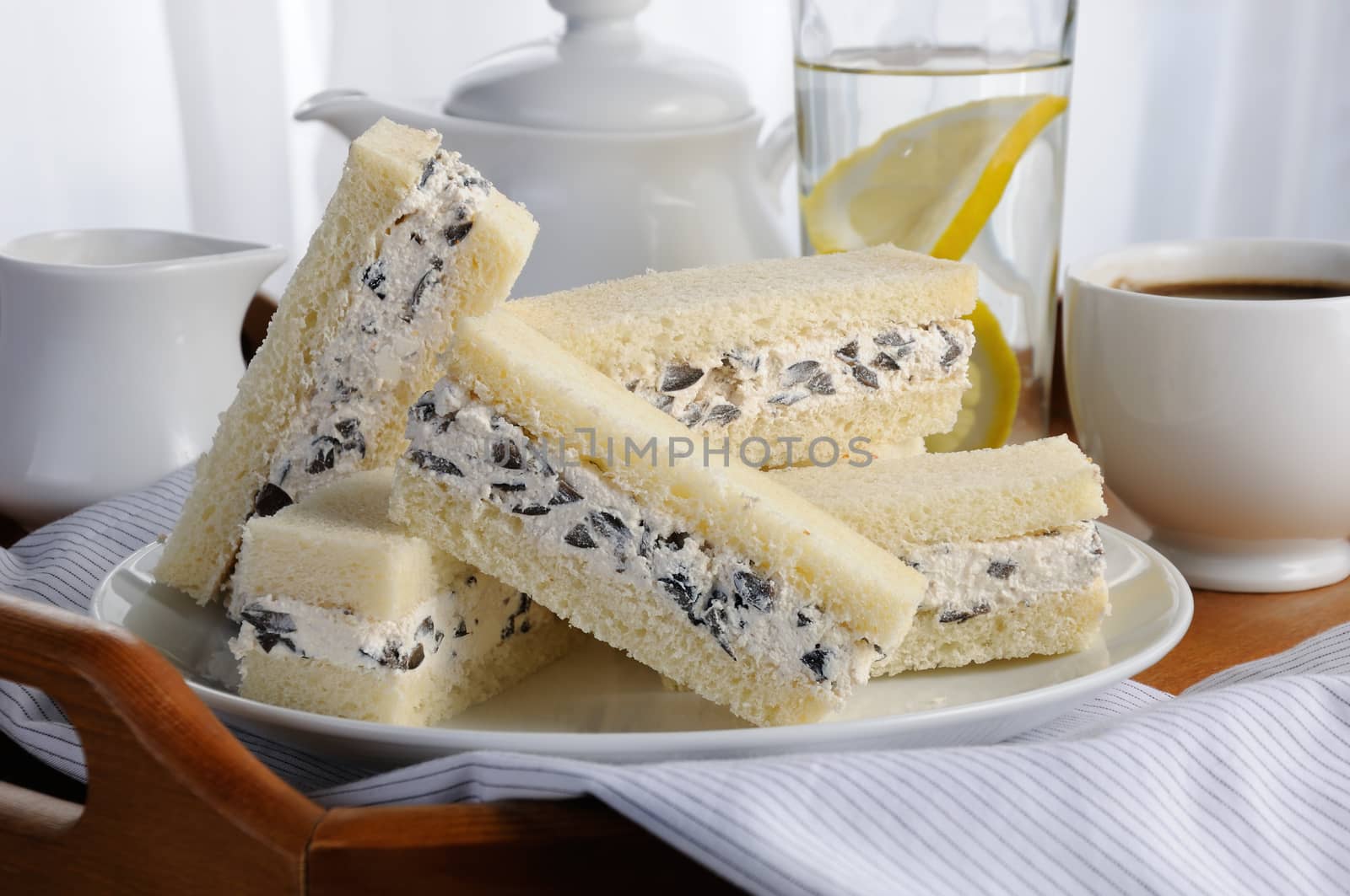 Slices of sandwich with ricotta and black olives on a plate, for breakfast with a cup of coffee