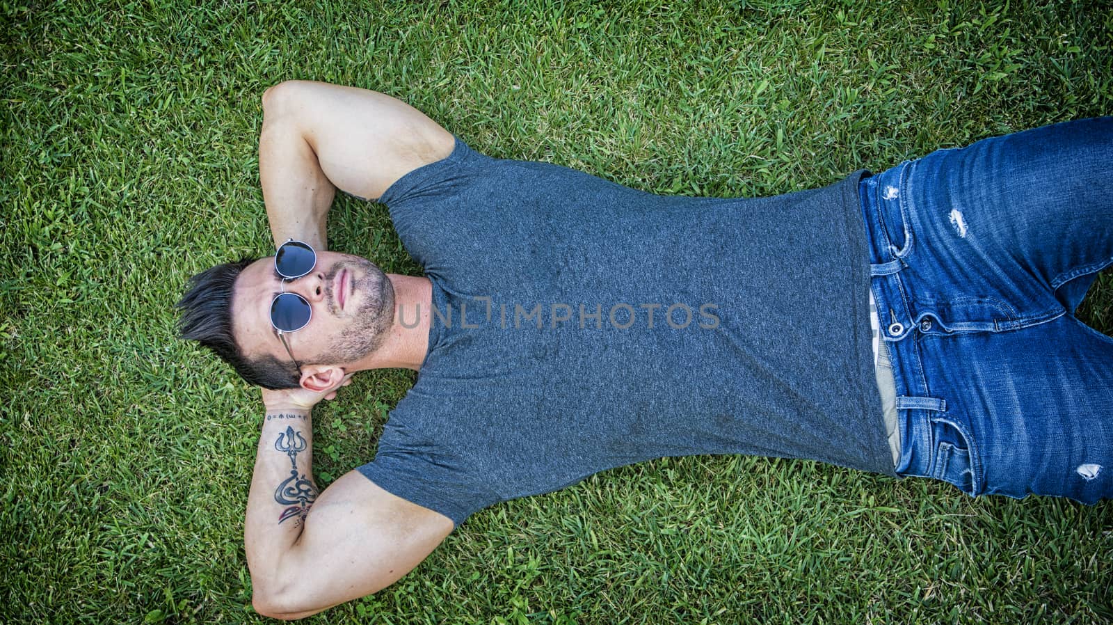 Good looking, fit male model relaxing lying on the grass, looking at camera, photographed right from above