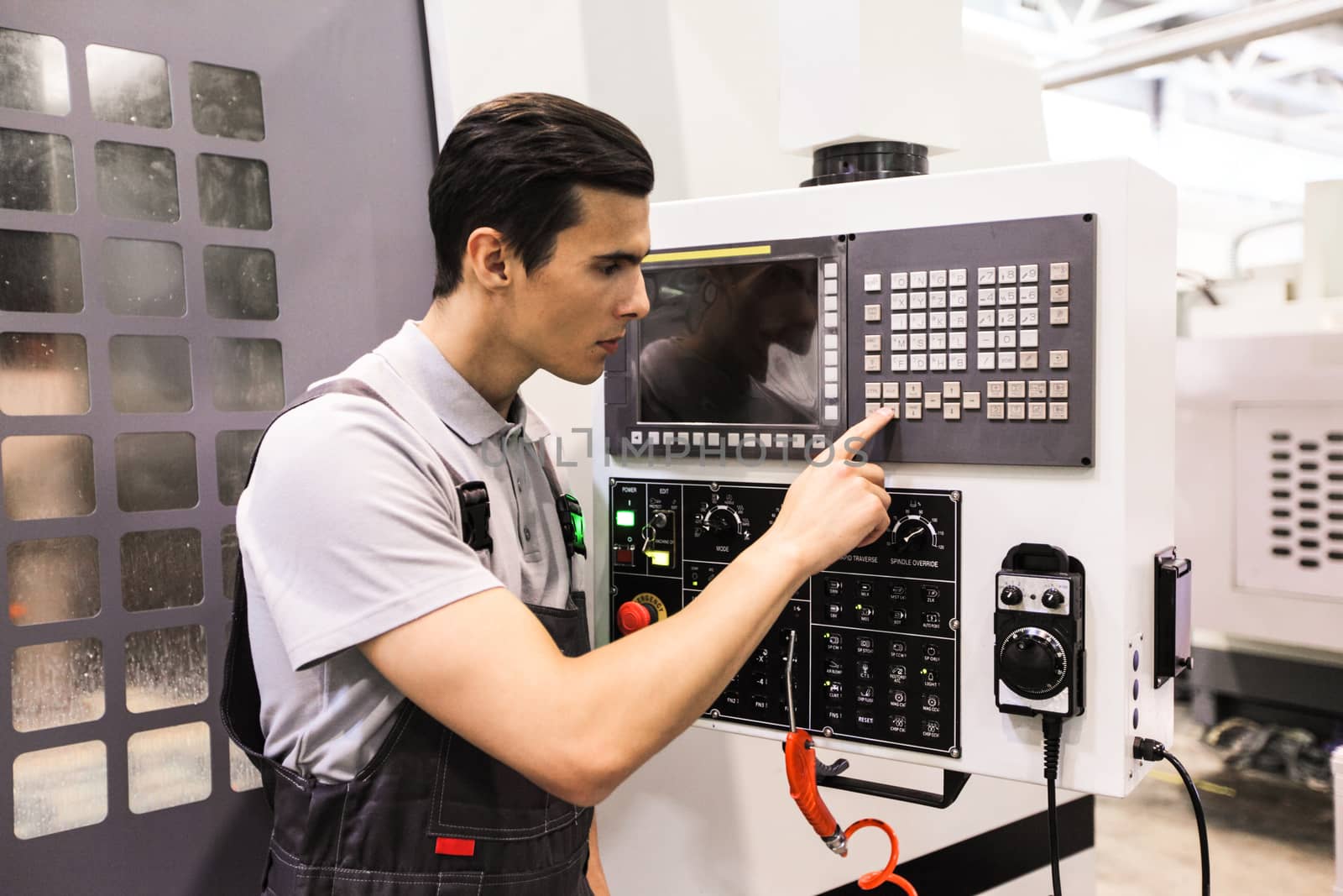 Worker pressing programming buttons on CNC machine control board in factory