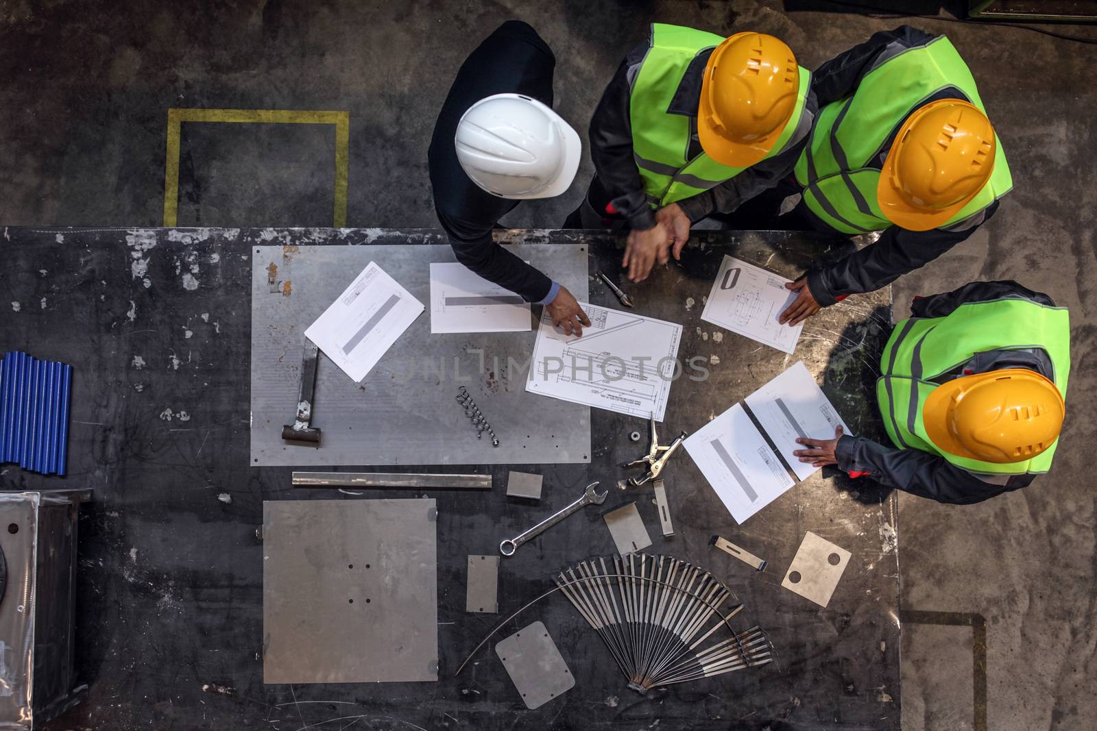 Workers and manager in safety helmets working with documents at factory
