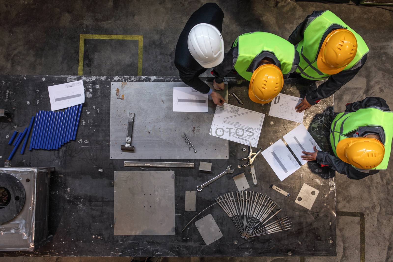 Workers and manager in safety helmets working with documents at factory